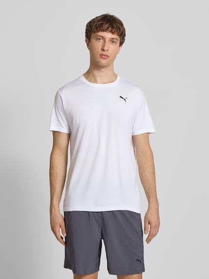 Męski model nosi TRAINING T-Shirt mit Label-Detail Modell od PUMA PERFORMANCE, krój regular fit, okrągły dekolt, krótki rękaw, biała gładka tkanina, przód całej sylwetki.