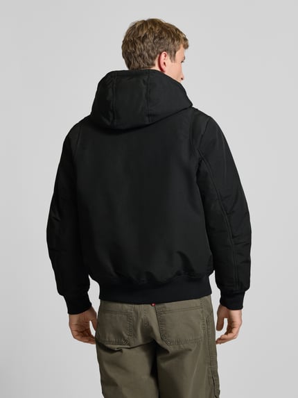 Męski model nosi czarną Jacke mit Kapuze und Eingrifftaschen Modell 'TRACE' od JACK & JONES, krój regular fit, widok z tyłu, długość tyłu w rozmiarze M: 70 cm, szerokość ramion w rozmiarze M: 46 cm, szerokość klatki piersiowej w rozmiarze M: 60 cm, długość rękawa w rozmiarze M: 68 cm