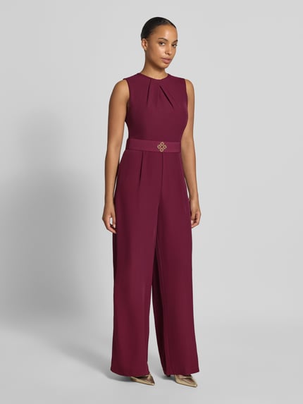 Vrouwenmodel draagt jumpsuit met stoffen riem van Rinascimento in bordeaux, materiaalmix met stretch, getailleerd, ronde hals, mouwloos, plooien, ritssluiting achter, ruglengte maat S 36 cm, borstwijdte 38 cm, totale lengte 149 cm, binnenbeenlengte 80 cm, effen kleur, gladde textuur, volledige lichaamsweergave van voren.