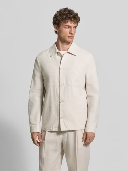 Männermodel trägt Relaxed Fit Overshirt aus Leinen-Baumwoll-Mix mit Kentkragen von MCNEAL, Knopfleiste, Brusttaschen, Sportmanschetten, Rückenlänge 69 cm, cremefarbener Stoff mit weicher Textur, Ganzkörperansicht von vorne.