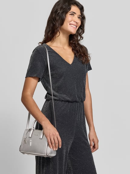 Frauenmodel trägt Umhängetasche mit Logo-Detail Modell 'LAILA XS' von MICHAEL MICHAEL KORS in Metallic-Optik, rechteckige Form, Ganzkörperansicht von vorne.