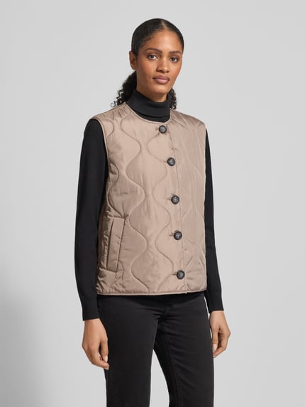 Frauenmodel trägt Regular Fit Steppweste mit einreihiger Knopfleiste Modell 'MILLIE' von Vero Moda, unifarbene Optik, seitliche Eingrifftaschen, gesteppte Textur, Ganzkörperansicht von vorne.