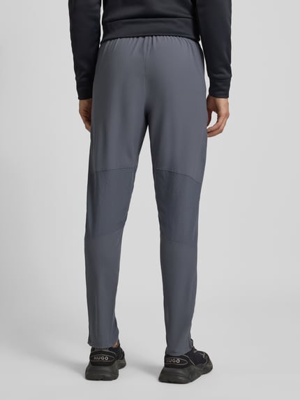 Männermodel trägt Trainingshose mit Reißverschlusstaschen von Under Armour, Regular-Fit, Elastikbund, grau, Ganzkörperansicht Rückansicht.