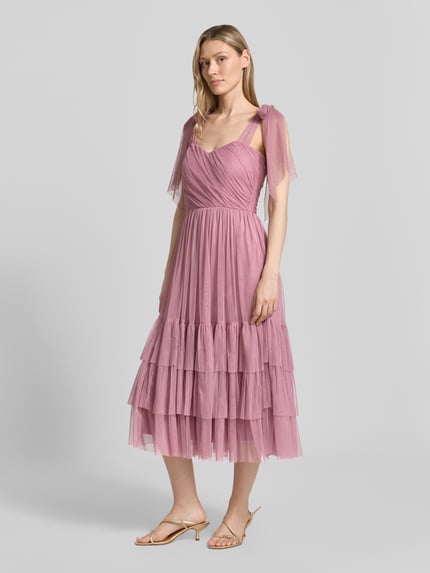 Frauenmodel trägt Knielanges Cocktailkleid im Stufen-Look von LACE & BEADS aus rosafarbenem Mesh, A-Linie, Drapierungen; Ganzkörperansicht von vorne. Rückenlänge bei Größe S: 104 cm, Brustweite: 40 cm.