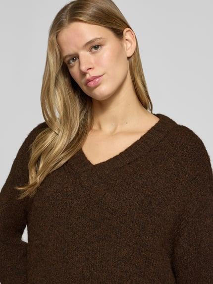 Frauenmodel trägt Pullover mit tiefem V-Ausschnitt von ONLY in Dunkelbraun, grob gestrickte Textur, Nahaufnahme Oberkörper, Damen Pullover von ONLY.