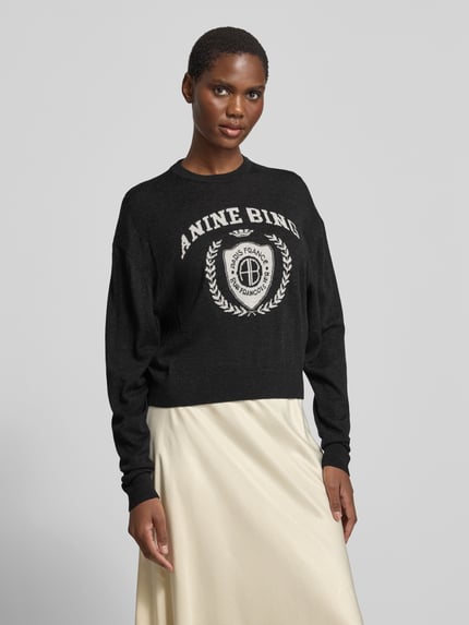 Frauenmodel trägt Sweatshirt mit Logo-Front Modell 'MIA SWEATER' von Anine Bing in schwarzer Melange-Optik, Motiv-Print, Feinstrick, Ganzkörperansicht von vorne.