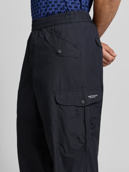 Männermodel trägt Wide Fit Cargo-Hose mit Baumwoll-Anteil von Armani Exchange, schwarz, elastischer Bund, Cargo-Taschen, Nahaufnahme Oberschenkel.