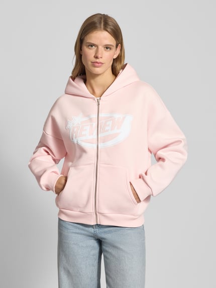 Frauenmodel trägt Sweatjacke mit Logo und Känguru-Tasche von Review, rosa Farbton, Baumwoll-Mix, Relaxed Fit, Ganzkörperansicht von vorne.
