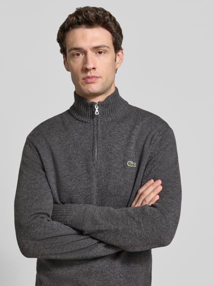 Männermodel trägt Troyer aus Wolle mit Logo-Patch von LACOSTE in uni Dunkelgrau, Strickstruktur, Regular Fit, Nahaufnahme Oberkörper.