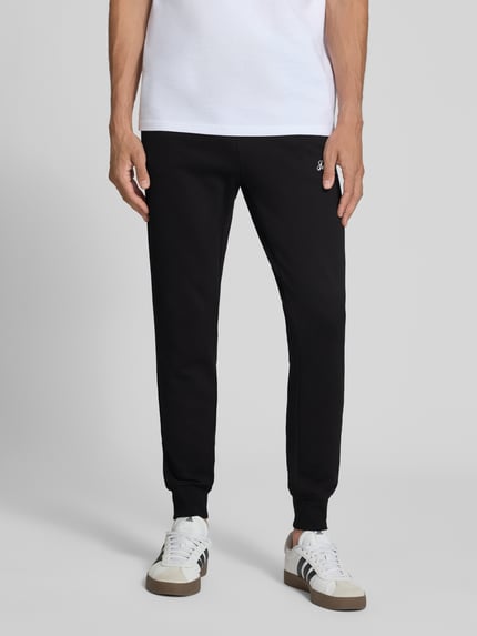 Männermodel trägt schwarze Sweatpants mit Label-Print Modell 'GORDON' von JACK & JONES, lockere Passform, Nahaufnahme Unterkörper.