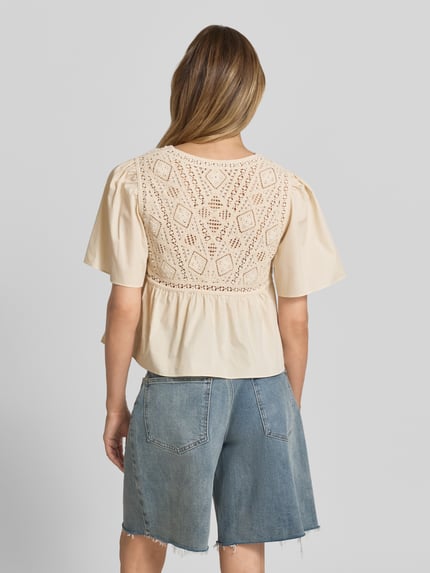 Vrouwenmodel draagt dames Blusentop met Häkelspitze model 'SALVI' van Bash, puur katoen, regular fit, v-hals, knoopsluiting, ruglengte 50 cm, mouwlengte 28 cm, beige tint, gehaakt kant op rug, gecombineerd met blauwe denim short, Ganzkörperansicht rückansicht.
