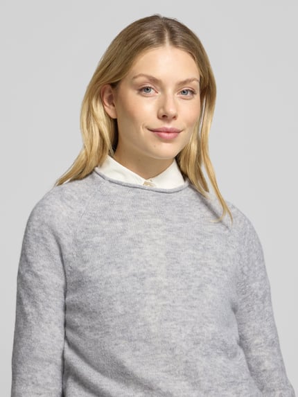 Frauenmodel trägt Pullover aus Alpaka Wolle mit Rippabschlüssen von BOSS Orange in hellgrauer Melange-Struktur, Feinstrick, Nahaufnahme Oberkörper.