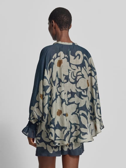 Männermodel trägt bluzka 'Bluse mit Schluppe und Volantärmeln' von Luisa Cerano, mieszanka lyocellu z dodatkiem ramii, krój loose fit, długość tyłu 74 cm, długość rękawów 65 cm, szerokie rękawy z marszczonym detalem, wzór w jasne i granatowe kwiatowe motywy, tekstura lekko przezroczysta, widok całej sylwetki z tyłu.