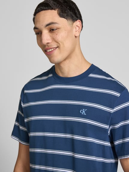 Männermodel trägt T-Shirt mit Logo-Stitching von Calvin Klein Jeans, Reine Baumwolle, Gerader-Schnitt, Rundhalsausschnitt, Nahaufnahme Oberkörper.