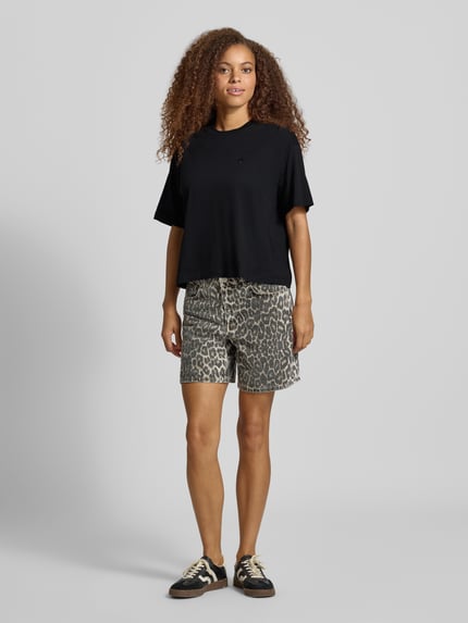 Frauenmodel trägt Regular Fit T-Shirt aus reiner Baumwolle Modell 'CHESTER' von Carhartt Work In Progress in Schwarz, Ganzkörperansicht von vorne. Damen T-Shirt, Stehkragen, Halbarm, Rückenlänge bei Größe S 56 cm.
