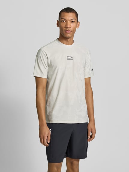 Männermodel trägt T-Shirt mit Rundhalsausschnitt und Label-Detail von EA7 Emporio Armani, Material-Mix mit Stretch-Anteil, Regular-Fit, dezente Musterung in Hellgrau, Ganzkörperansicht von vorne. Rückenlänge bei Größe M: 69 cm.