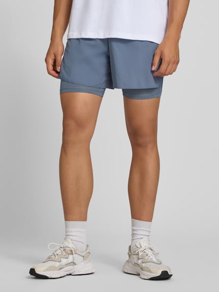 Mannelijk model draagt Regular fit sportshorts met logoprint model 'ADI365/// 2i1 M' van adidas Training, blauwgrijze tinten, geheel vooraanzicht.