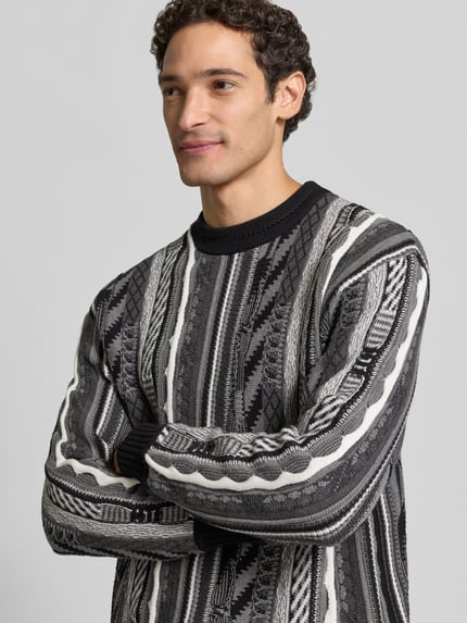 Männermodel trägt Regular Fit Strickpullover aus reiner Baumwolle von COLUCCI in Schwarz-Grau mit Stehkragen und gerippten Abschlüssen, Nahaufnahme Oberkörper.