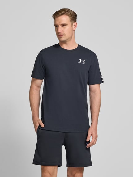 Mannenmodel draagt Regular Fit T-shirt met logo-stitching model 'Icon' van Under Armour van katoenmix in zwart met ronde hals, ruglengte bij maat M 72 cm, ganzekörperaanzicht van voren.
