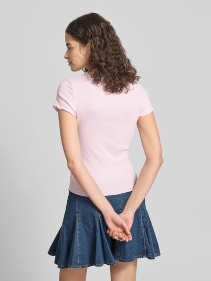 Frauenmodel trägt Slim Fit T-Shirt aus Baumwoll-Mix von Tommy Hilfiger in Hellrosa mit Frill-Ärmeln und Rundhals zu Jeansrock, Ganzkörperansicht Rückansicht.