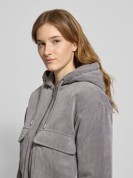Frauenmodel trägt Regular Fit Bomberjacke mit Kapuze Modell 'SUVA' von Only aus grauem Cord, gestreifte Struktur, Label Stitching, Nahaufnahme Oberkörper.