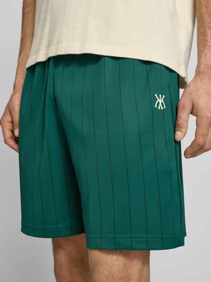 Männermodel trägt Herren Shorts mit elastischem Bund Modell 'Insignia Shadow' von KARL KANI im Allover-Look, grün, Nahaufnahme Oberschenkel. Bundweite bei Größe M: 38 cm, Innenbeinlänge: 19 cm, Regular-Fit.