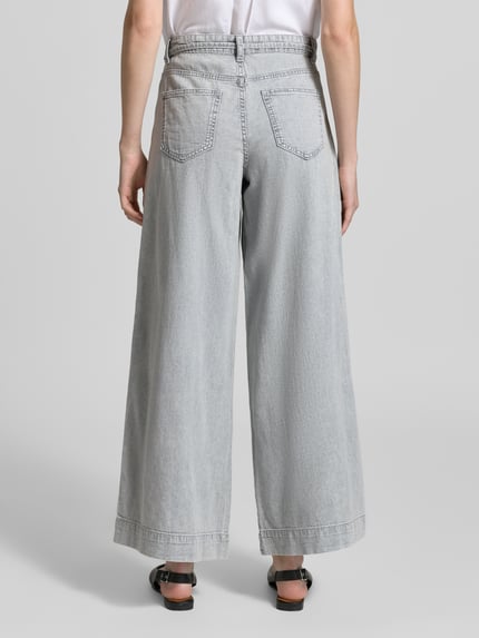 Männermodel trägt Regular Fit Wide Leg Jeans aus reiner Baumwolle Modell 'AISA' von Vero Moda w jasnoszarym kolorze, denim, tekstura twillu, pięć kieszeni, szlufki na pasek, zapięcie na guzik i kryty zamek, widok całej sylwetki z tyłu.