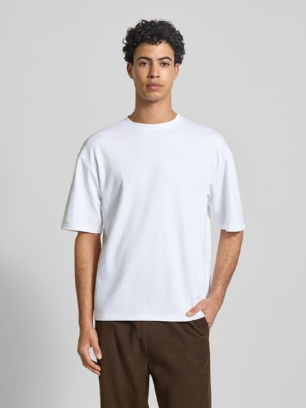 Męski model nosi Boxy Fit T-Shirt aus Baumwoll-Mix Modell 'CASPIAN AIRFLEX BOXY' von Only & Sons, efekt: jednolity kolor, oddychający materiał, chłodząca, z regulacją wilgoci, okrągły dekolt, krótki rękaw, mieszanka bawełny, ganzkörperansicht von vorne.