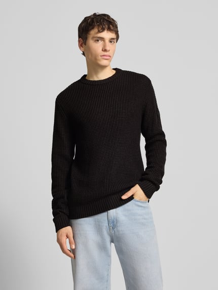 Männermodel trägt schwarzen Strickpullover mit gerippten Abschlüssen Modell 'LIAM' von Jack & Jones, Regular Fit, Ganzkörperansicht von vorne.