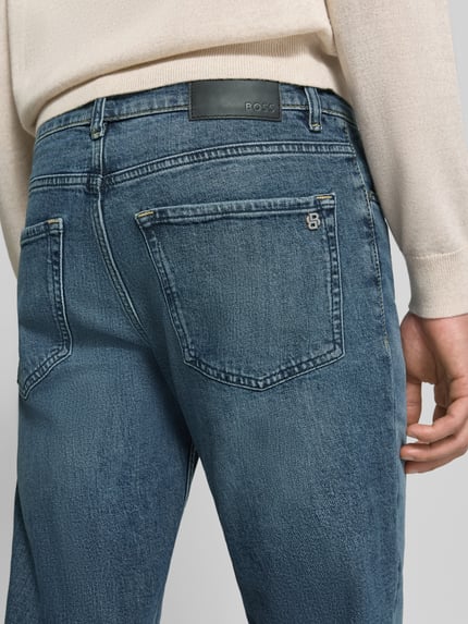 Männermodel trägt Regular Fit Jeans mit Used Waschung Modell 'ONYX SMU' von BOSS Orange im Medium Wash Denim, Nahaufnahme Rückansicht.
