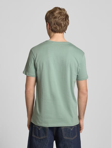 Männermodel trägt T-Shirt mit Logo und Rundhalsausschnitt von Alpha Industries in Grün, Reine Baumwolle, Regular-Fit, Rückenlänge 67 cm, Ganzkörperansicht Rückansicht.