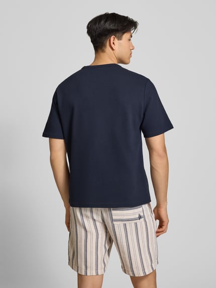 Männermodel trägt T-Shirt mit Label-Stitching von REVIEW, Baumwoll-Mix in Dunkelblau, Waffelstruktur, gerader Schnitt, Ganzkörperansicht Rückansicht.