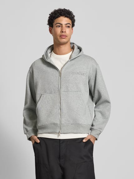 Männermodel trägt Sweatjacke mit Kapuze von ANOTHER COTTON LAB, hellgrauer Baumwoll-Mix, lockerer Schnitt, Front-Reißverschluss, Ganzkörperansicht von vorne.