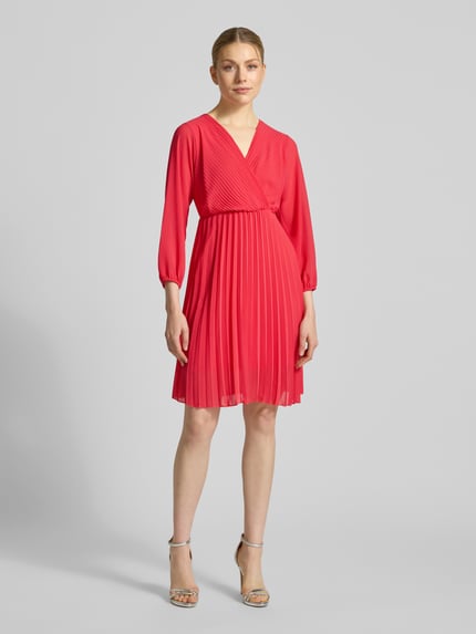 Frauenmodel trägt knielanges Kleid mit Plisseefalten Modell 'Im44sa' von ZABAIONE in Rot, taillierter Schnitt, Wickel-Optik, Ganzkörperansicht von vorne.