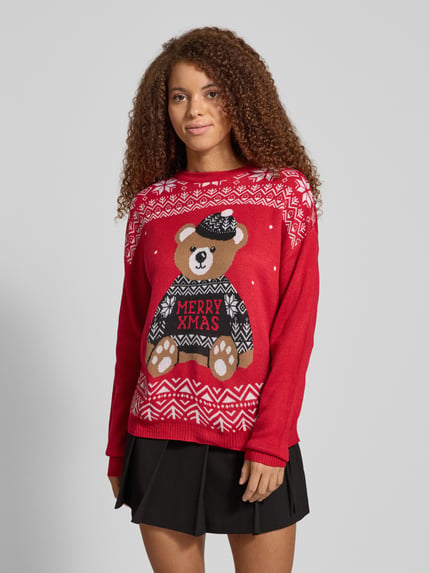 Frauenmodel trägt Regular Fit Strickpullover mit Weihnachtsmotiv Modell 'TEDDY' von Only, rot mit grafischem Muster, Rundhals, Langarm, Stricktextur, unifarben, Intarsien-Details, Label Stitching, Ganzkörperansicht von vorne.
