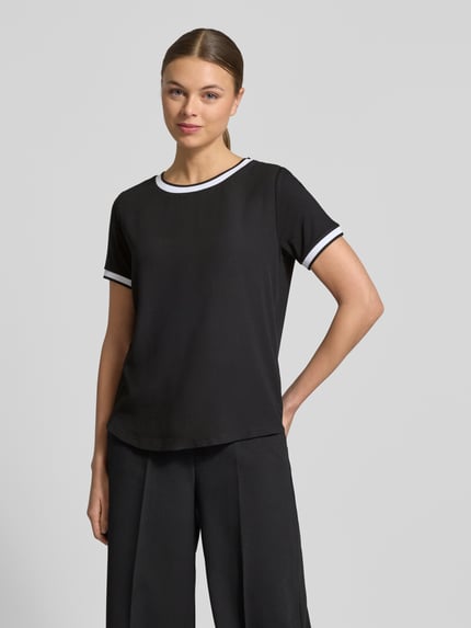 Modelka nosi Regular Fit T-Shirt aus Viskose-Mix von More & More, czarny kolor, elastyczny materiał, krój regular fit, okrągły dekolt, krótkie rękawy, długość tyłu w rozmiarze 36: 57 cm, ujęcie całej sylwetki z przodu.