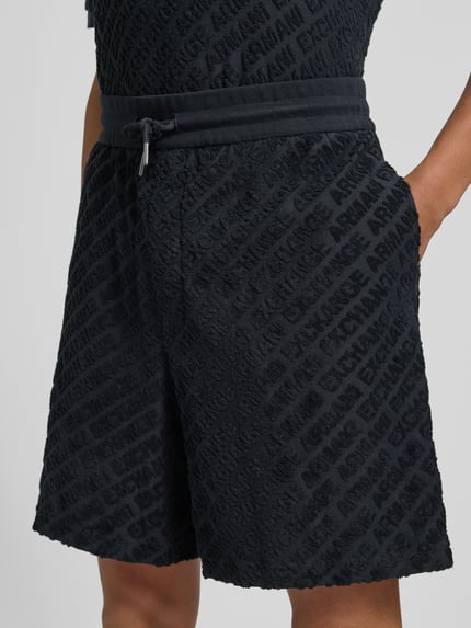 Männermodel trägt Shorts mit Logo-Muster und elastischem Bund von ARMANI EXCHANGE, katoen-elastaanmix, regular fit, zwart, logo patroon, elastische tailleband, geheelopname voorkant