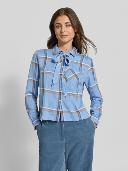 Frauenmodel trägt Regular Fit Schluppenbluse mit Brusttasche von MORE & MORE in hellblau mit Karomuster, Ganzkörperansicht von vorne. Damen Schluppenbluse mit Schluppe, aufgesetzte Brusttasche, durchgehende Knopfleiste, langärmliges Design, Rückenlänge 59 cm, Ärmellänge 65 cm.