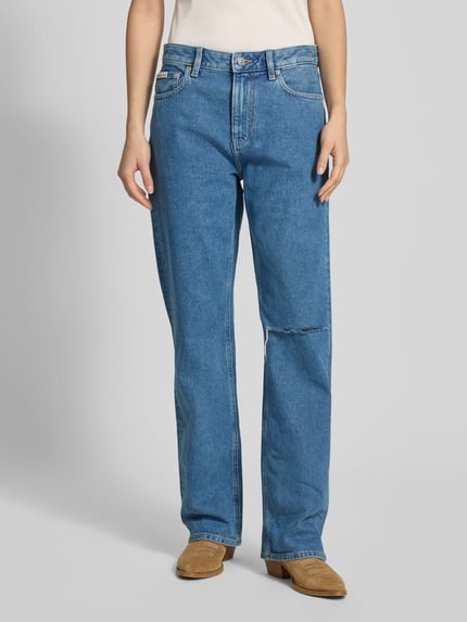 Frauenmodel trägt Straight Fit Jeans im Destroyed-Look von Calvin Klein Jeans in Mittelblau, mit sichtbarem Label-Detail, Ganzkörperansicht von vorne.