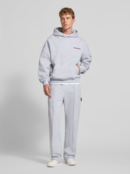 Männermodel trägt Relaxed Fit Hoodie aus Baumwoll-Mix mit Label-Detail von PROHIBITED, hellgrau, mit Känguru-Tasche, elastische Abschlüsse, Ganzkörperansicht von vorne.