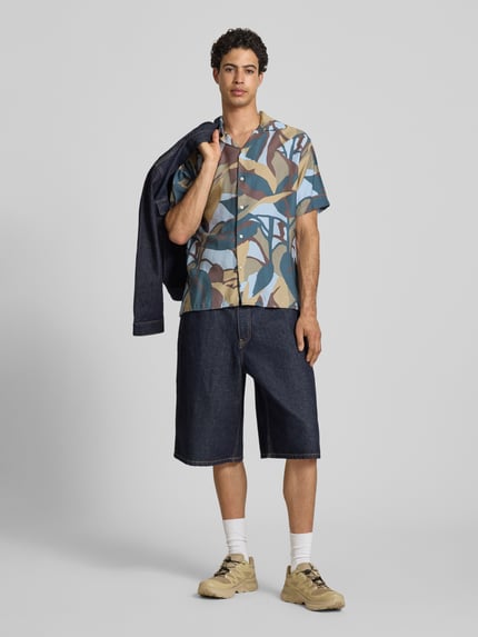 Männermodel trägt Regular Fit Freizeithemd im Allover-Look Modell 'TAVIRA MARSHALL' von Jack & Jones in Blau-, Beige- und Grüntönen, kombiniert mit dunkler Jeansshorts, Viskose-Mix, Reverskragen, Nahaufnahme Ganzkörperansicht von vorne.