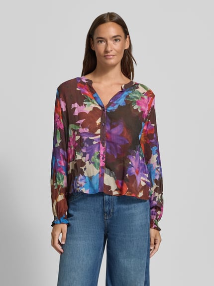 Vrouwenmodel draagt Regular Fit Bluse aus Viskose-Mix mit V-Ausschnitt van Milano Italy, Dames blouse met all-over look, knoopsluiting, ruglengte bij maat 36: 54 cm, mouwlengte bij maat 36: 61 cm, kleurrijke bloemenmotieven, Ganzkörperansicht van voren.