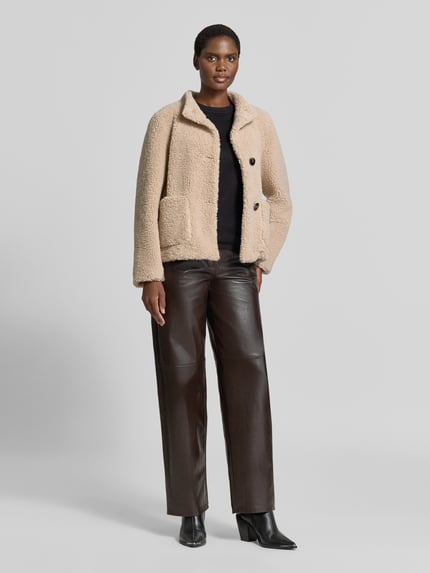 Kobieta modelka nosi Regular Fit Jacke mit Stehkragen von Fuchs Schmitt z Futerko, krój regular fit, stójka, nakładane kieszenie, listwa guzikowa, długość tyłu w rozmiarze 36: 59 cm, szerokość ramion w rozmiarze 36: 43 cm, szerokość klatki piersiowej w rozmiarze 36: 52 cm, długość rękawów w rozmiarze 36: 63 cm; jasnobeżowa, z teksturą futerka, prostokątne kieszenie, widoczne dwa guziki, cała sylwetka z przodu.