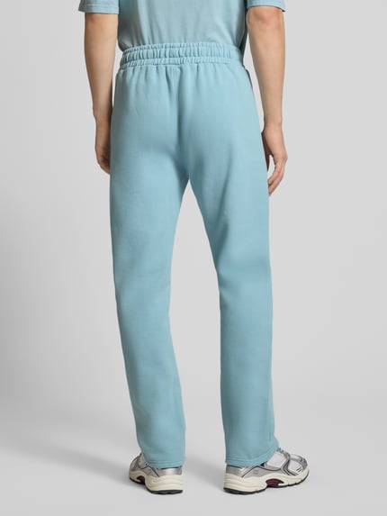 Männermodel trägt hellblaue Sweathose mit elastischem Bund von Pegador, Baumwoll-Mix, lockerer Schnitt, Label-Stitching, Ganzkörperansicht Rückansicht.