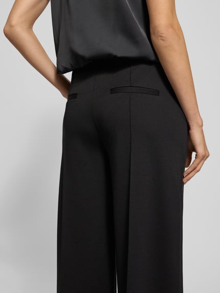Frauenmodel trägt Wide Leg Stoffhose mit fixierten Bügelfalten Modell 'KATE' von ICHI, dunkles Material-Mix mit Viskose-Anteil, Paspeltaschen am Gesäß, Ganzkörperansicht Rückansicht.