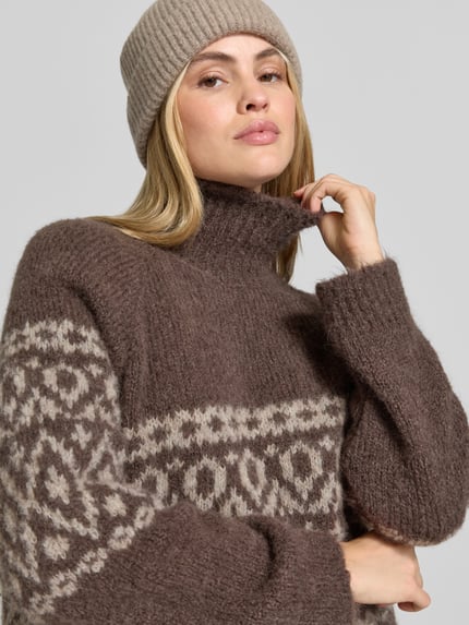 Frauenmodel trägt Pullover aus Alpaka mit Rollkragen Modell 'CRISTINE' von BAUM & PFERDGARTEN in brauner Strickoptik mit geometrischem Jacquardmuster, gerippte Abschlüsse, Nahaufnahme Oberkörper.