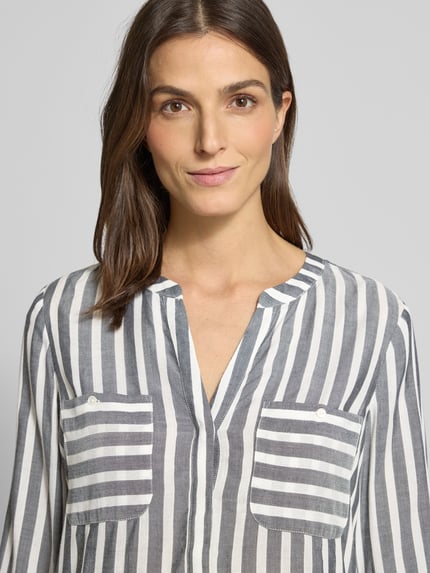 Frauenmodel trägt Blusenshirt mit Streifenmuster von TOM TAILOR aus reiner Viskose, Loose-Fit, V-Ausschnitt, Brusttaschen, Nahaufnahme Oberkörper.