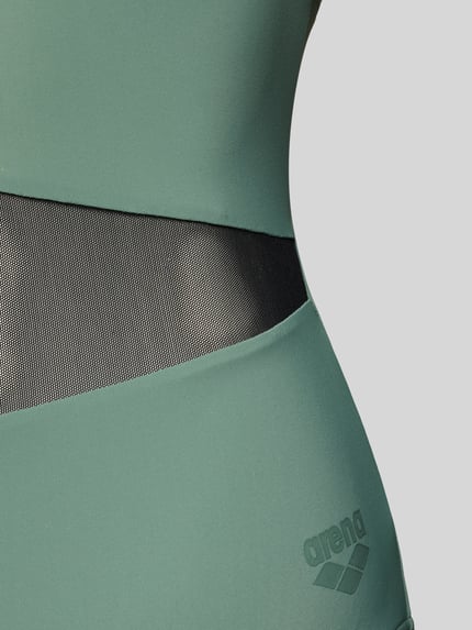 Kobieta nosi Slim Fit Badeanzug mit semitransparenten Partien od Arena, elastyczna mieszanka materiałów, siateczka, krój bez rękawów, detal, zbliżenie na boczną część talii.