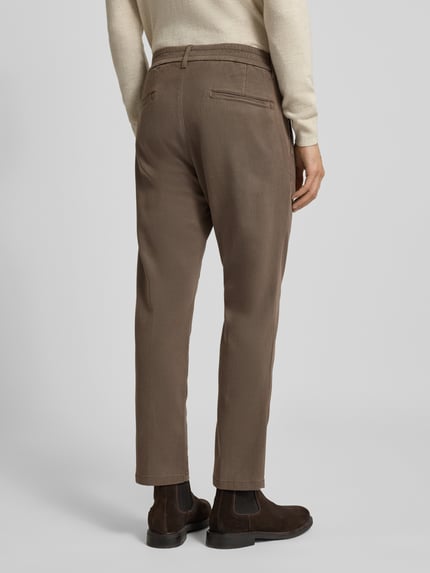 Männermodel trägt Regular Fit Hose mit Bundfalten Modell 'CHASY' von Drykorn in Braun, Lyocell-Baumwoll-Mix mit Stretch-Anteil, Ganzkörperansicht Rückansicht.