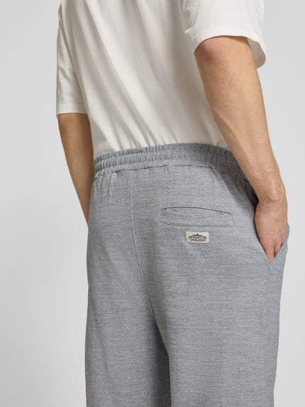Männermodel trägt Track Pants mit Logo-Stitching Modell 'Skagen' von Pegador aus Reine Baumwolle, Loose-Fit, Gesäßleistentasche, Nahaufnahme Rückansicht.